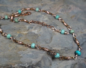May include: A copper chain necklace with turquoise beads. The necklace is on a grey textured surface.