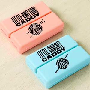 May include: Two rectangular craft caddies, one peach and one light blue. The peach caddy reads "LITTLE KNITTING CADDY" with a yarn ball and needles graphic. The blue caddy reads "LITTLE CROCHET CADDY" with a yarn ball and crochet hook graphic.