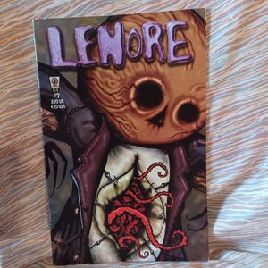 May include: A comic book cover with the title "LENORE" in purple lettering. The illustration shows a character with a wooden mask and a red, tentacle-like design. The comic is issue #7.