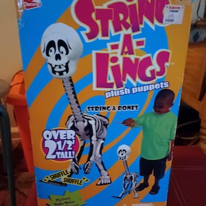 May include: A String-A-Lings plush puppet box with a skeleton design. The box is blue and orange with the words "String-A-Lings" in pink. The puppet is over 2 1/2 feet tall. The box also has the words "String & Bones" and "plush puppets".