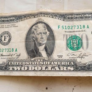 May include: A two dollar bill with a portrait of Thomas Jefferson, the text "F 51027318 A" and "WASHINGTON, D.C." printed on it. The bill is from the series 1976.
