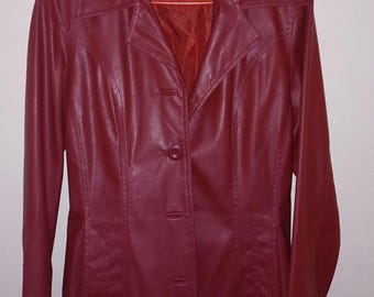 May include: A dark red jacket with a smooth finish, featuring a pointed collar, long sleeves, and a front button closure. The interior label displays the text BLUE ROSE. The jacket is displayed on an orange plastic hanger against a plain wall.