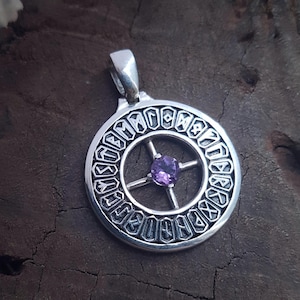 May include: Silver pendant with a circular design featuring runes and a central purple gemstone. The pendant has a loop for a chain and is set against a dark, textured background.