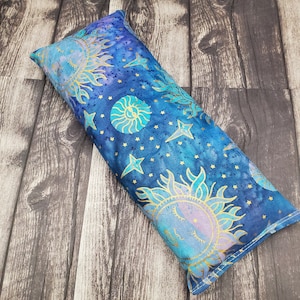 May include: A blue and gold fabric pillow with a sun and moon design. The pillow is filled with buckwheat hulls and is perfect for neck support.