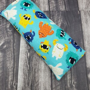 May include: A blue eye pillow with a colorful monster print. The pillow is filled with flax seeds and lavender.