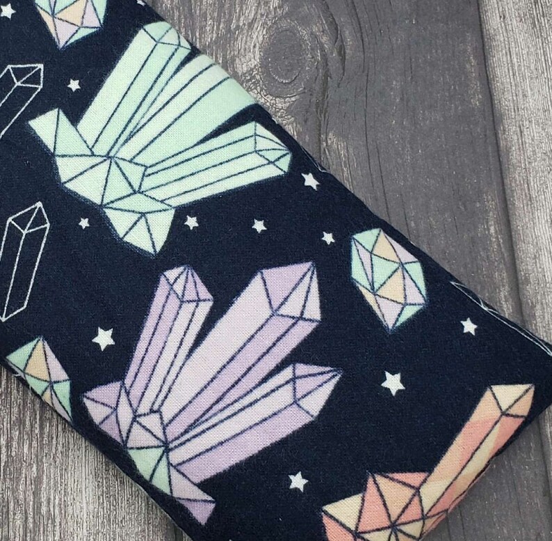 May include: A dark blue fabric eye pillow with a repeating pattern of pastel coloured crystals and white stars.