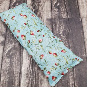 May include: A light blue eye pillow with a floral pattern of red flowers and green leaves.