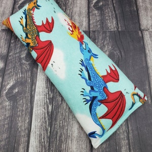 May include: A blue and red dragon with fire coming out of its mouth on a light blue background with white clouds. The dragon is on a long rectangular pillow.