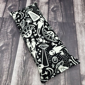 May include: A black and white rectangular pillow with a repeating pattern of aliens, UFOs, and stars. The pillow is made of fabric and has a white seam around the edges.