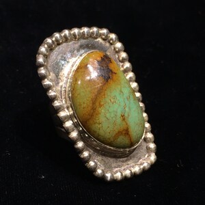 Pu&ograve; includere: Un anello d'argento con una pietra ovale di turchese verde e marrone incastonata in una montatura a perline.