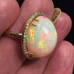 Op de afbeelding: Een gouden ring met een grote ovale opaal-edelsteen omringd door een halo van kleine diamanten.
