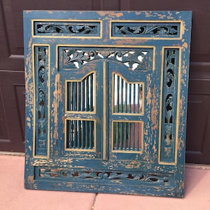 May include: A distressed teal blue wooden windowpane with carved floral details and a gold trim. The windowpane has a mirror behind the carved wood.