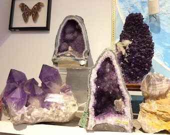 May include: A collection of amethyst crystals in various shapes and sizes. Some crystals are in the form of geodes, while others are clusters of points. The crystals are a deep purple color and have a natural, rough texture.