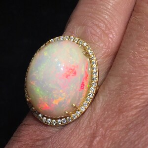Op de afbeelding: Een gouden ring met een grote ovale opaal-edelsteen omringd door een halo van kleine diamanten.