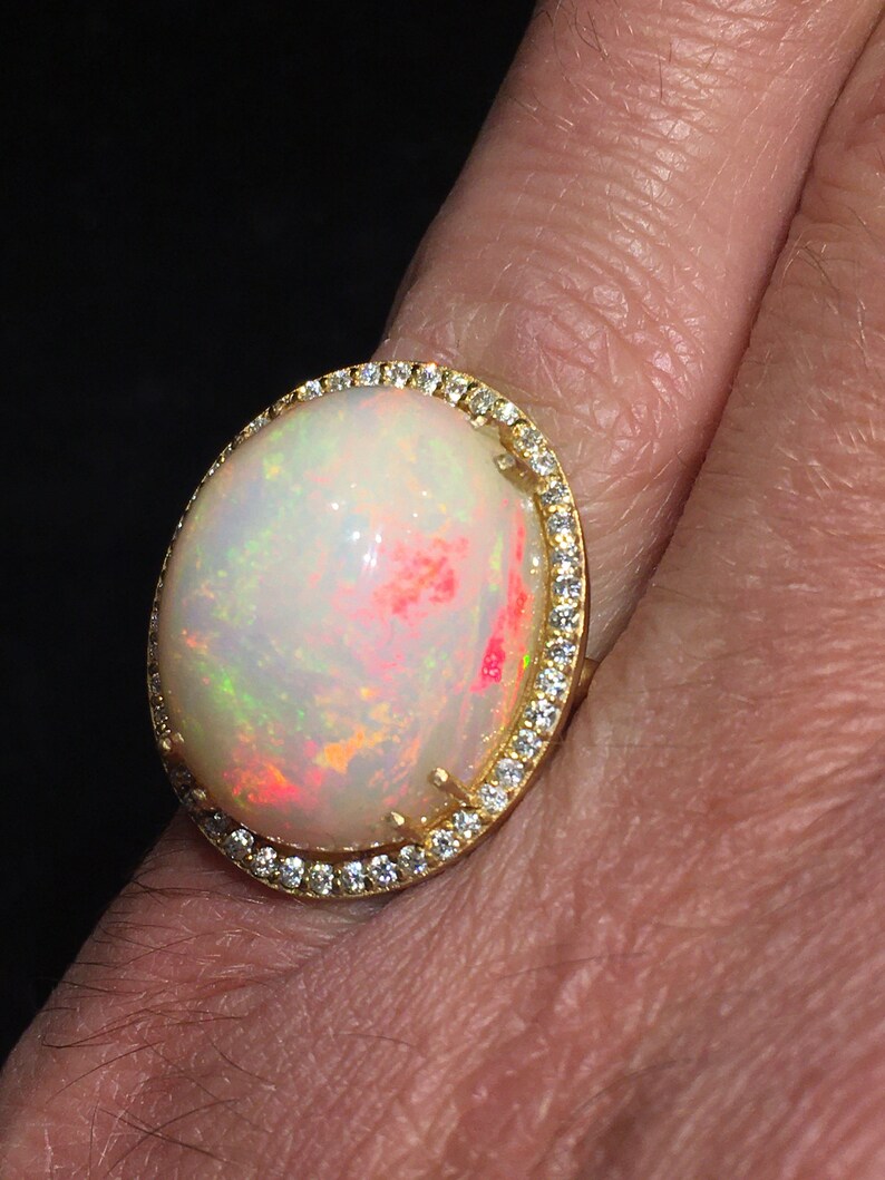 Op de afbeelding: Een gouden ring met een grote ovale opaal-edelsteen omringd door een halo van kleine diamanten.