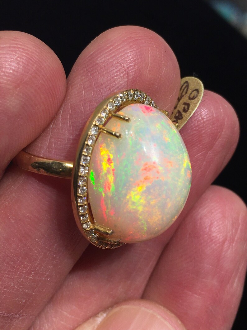 Op de afbeelding: Een gouden ring met een grote ovale opaal-edelsteen omringd door een halo van kleine diamanten.