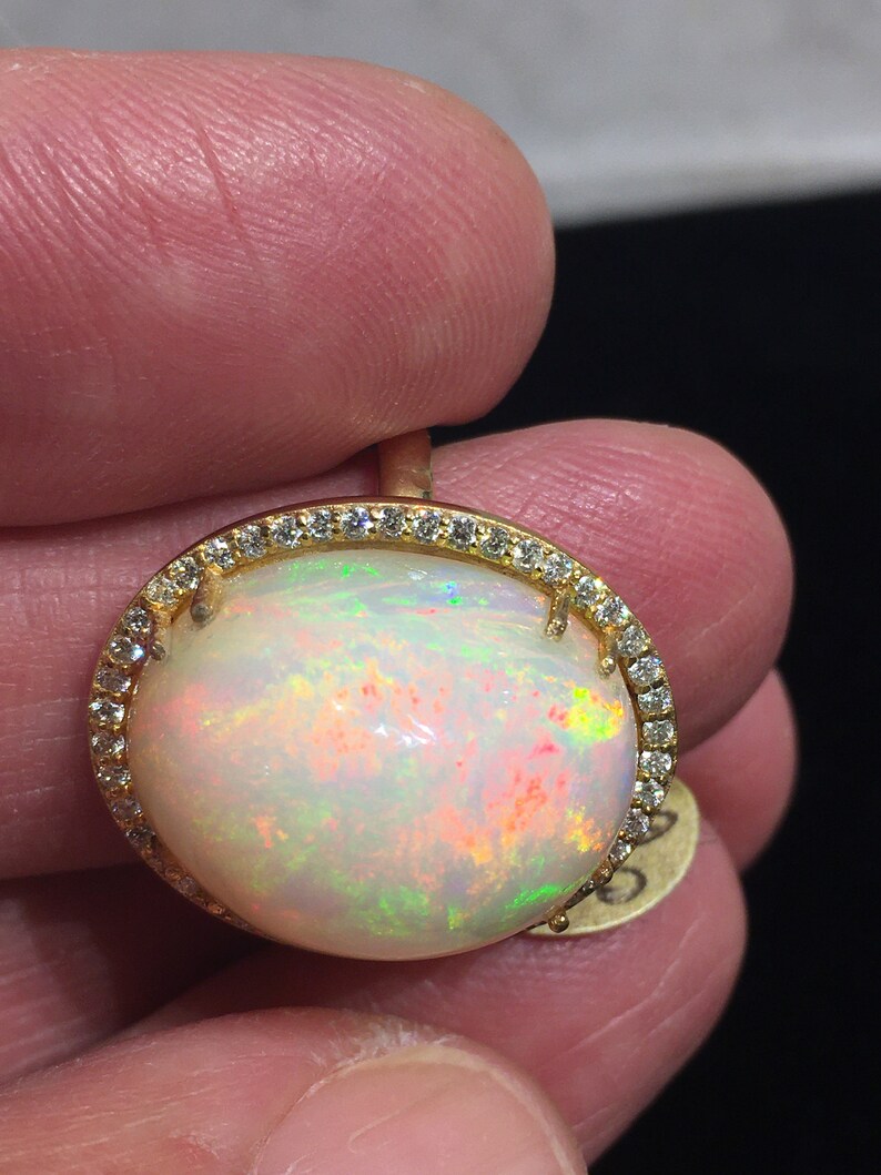 Op de afbeelding: Een gouden ring met een grote ovale opaal-edelsteen omringd door een halo van kleine diamanten.