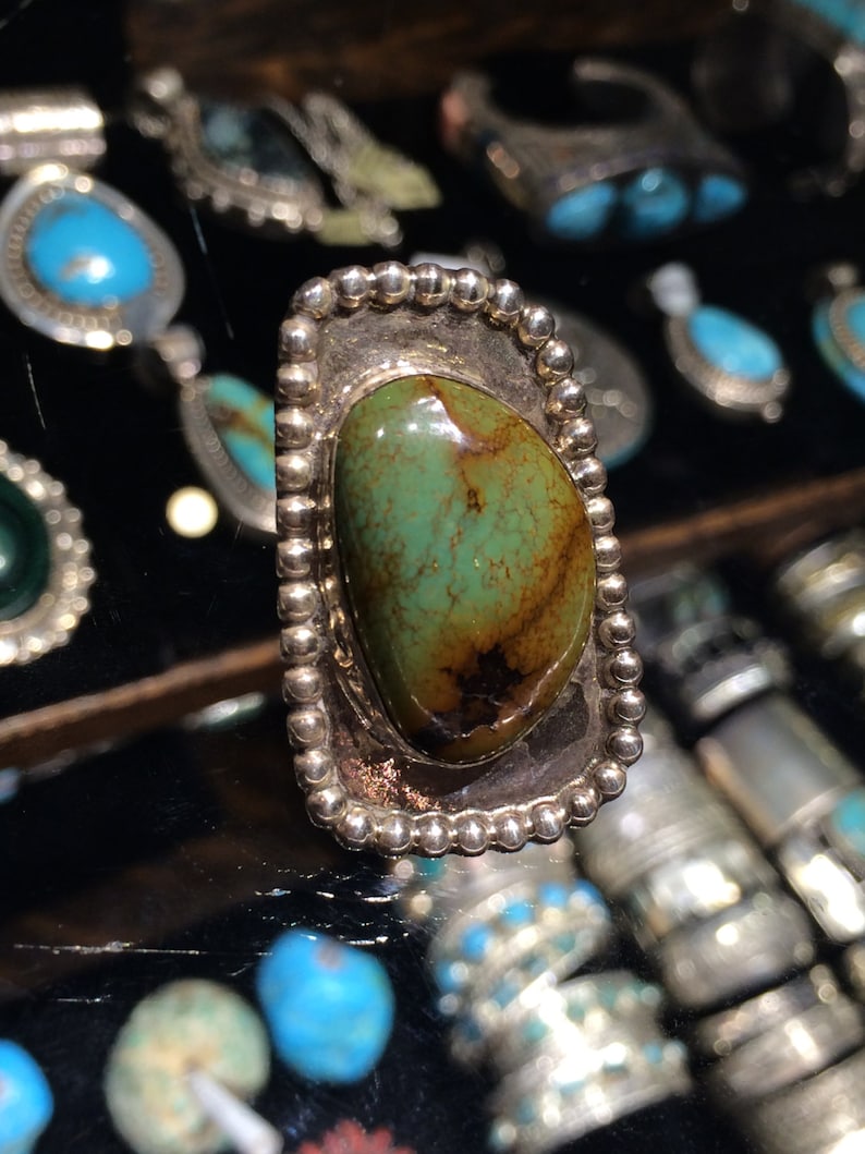 Pu&ograve; includere: Un anello d'argento con una pietra turchese verde e marrone incastonata in una montatura a perline.