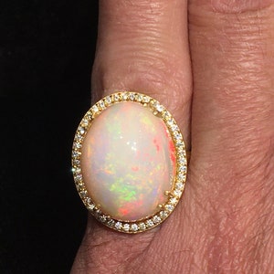 Op de afbeelding: Een gouden ring met een grote ovale opaal-edelsteen omringd door een halo van kleine diamanten.
