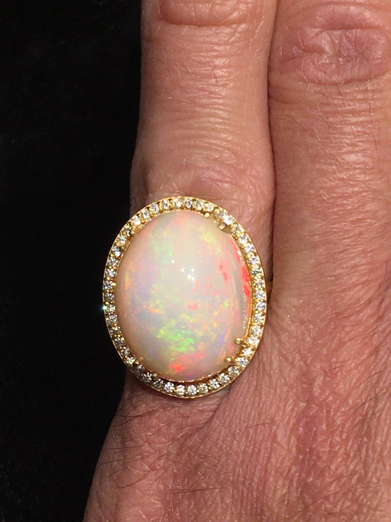 Op de afbeelding: Een gouden ring met een grote ovale opaal-edelsteen omringd door een halo van kleine diamanten.
