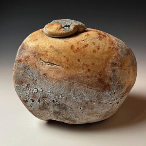 May include: A round, ceramic jar with a lid. The jar is a mottled brown and gray color with a rough, textured surface.