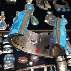 May include: A silver cuff bracelet with turquoise inlay. The bracelet is decorated with a geometric pattern and has a silver band with the inscription "BWB STERLING".