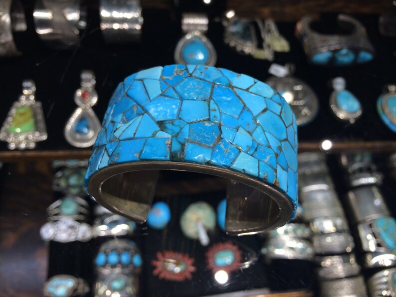 May include: A turquoise cuff bracelet made of many small, irregular pieces of turquoise set in silver. The bracelet is wide and has a rounded shape.