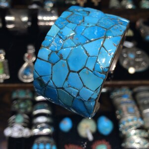 May include: A turquoise blue bracelet made of many small, irregular pieces of turquoise. The bracelet is wide and has a smooth, polished finish.