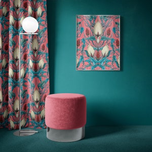 Op de afbeelding: Een roze fluwelen poef met een zilveren basis staat voor een turquoise muur met een ingelijst afdruk van roze en groene bloemenkunst. De afdruk heeft een symmetrisch ontwerp van witte bloemen met rode bessen.
