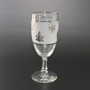 May include: A clear champagne flute with a frosted band featuring silver leaf designs. The rim and base of the frosted band are trimmed with silver. The stem and base of the glass are clear.