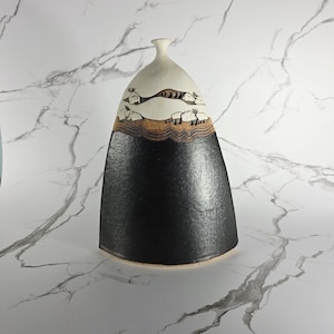 May include: A ceramic vase with a unique, asymmetrical shape. The top portion is off-white, transitioning to a band of tan and brown, and then to a textured black base. The design includes stylized mountain and cloud motifs.