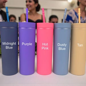 Puede incluir: Cinco vasos de colores con pajitas se muestran sobre una superficie blanca. Los vasos son en tonos Azul Medianoche, Morado, Rosa Fucsia, Azul Polvoriento y Beige. Cada vaso tiene una pajita del mismo color y el nombre del color impreso.