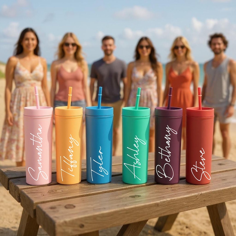Puede incluir: Seis vasos de colores con pajitas est&aacute;n colocados sobre una mesa de madera en la playa. Cada vaso es de un color diferente: rosa, naranja, azul, verde, morado y rojo. Cada vaso tiene un nombre en escritura blanca: Samantha, Tiffany, Tyler, Ashley, Bethany y Steve.