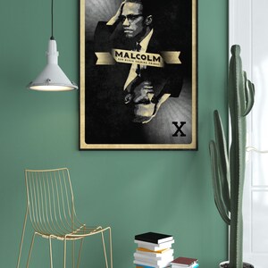 May include: A black and white poster with a portrait of Malcolm X. The poster is framed in black and has a gold ribbon with the text "Malcolm, Our Black Shining Prince". The poster is hanging on a green wall.