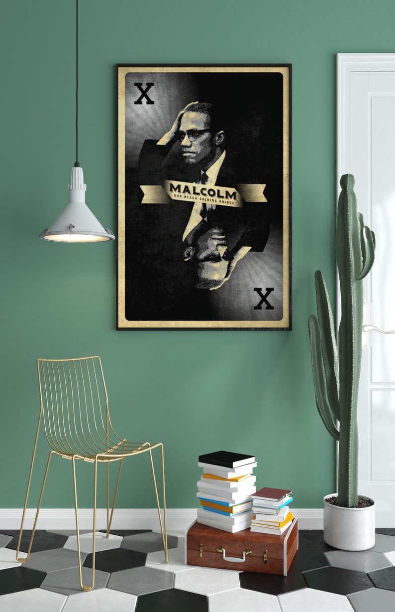May include: A black and white poster with a portrait of Malcolm X. The poster is framed in black and has a gold ribbon with the text "Malcolm, Our Black Shining Prince". The poster is hanging on a green wall.
