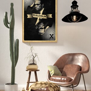 May include: A black and white poster with a portrait of Malcolm X. The poster is framed in a light wood frame and has the text "Malcolm X Our Black Guiding Prince" and an "X" in each corner.