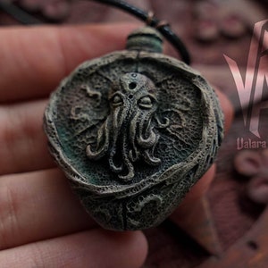 May include: A dark green and brown pendant necklace featuring a detailed sculpted image of Cthulhu, a fictional tentacled creature from the works of H.P. Lovecraft.