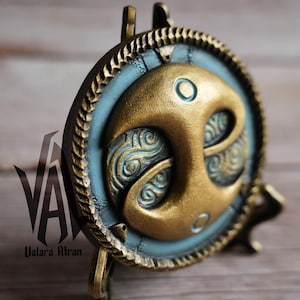 May include: A gold and blue decorative wall hanging with a stylized design of a crescent moon with swirling patterns. The hanging is on a small stand.