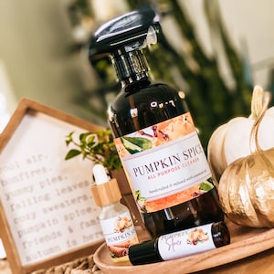Op de afbeelding: Een verzameling herfstproducten, waaronder een spuitfles, een kleine druppelfles en een rollerfles, allemaal met het label "Pumpkin Spice". De spuitfles is donkerbruin met een zwarte spuitkop. De flessen staan op een houten dienblad.