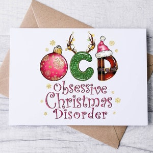 May include: A white greeting card with the text "OCD Obsessive Christmas Disorder" in a festive design. The letters are decorated with Christmas ornaments, antlers, and a Santa hat. The card is on a brown envelope.