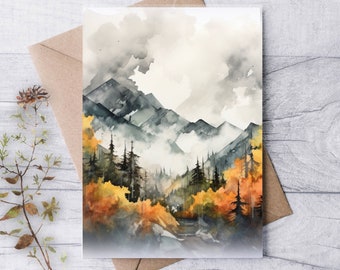 Könnte beinhalten: Aquarell-Kunstdruck mit einer Bergkette, immergrünen Bäumen und Herbstlaub in Grau-, Gelb- und Orangetönen. Das Kunstwerk befindet sich auf einer weißen Karte, mit einem braunen Umschlag dahinter. Ein Zweig getrockneter Blumen befindet sich links.
