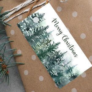 May include: A gift tag with a watercolor forest design and the words "Merry Christmas" in script. The tag is attached to a brown polka-dot wrapped gift with a twine bow.