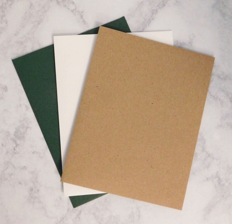 May include: Three rectangular sheets of paper in different colors: dark green, white, and brown. The sheets are arranged in a layered, overlapping fashion, with the brown sheet on top. The paper has a smooth, matte finish.