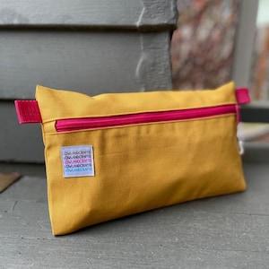 May include: A mustard yellow zippered pouch with a hot pink zipper and a small label that reads "Owl and Crafts" in pink, blue, and white lettering.