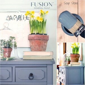 May include: A gray painted dresser with two drawers and a black ring pull handle. The dresser is decorated with a potted plant, books, and a glass cloche. The paint color is labeled "Soap Stone" and is a product of Fusion Mineral Paint.
