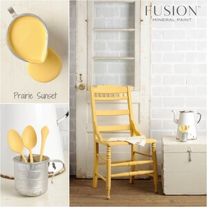 May include: A yellow chair painted with Fusion Mineral Paint in the color Prairie Sunset. The chair has a simple design with a back and four legs. The chair is sitting on a wooden floor in front of a white brick wall.