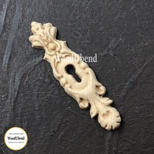 May include: A wooden keyhole cover with intricate details and a decorative design. The cover is unfinished and ready to be painted or stained.