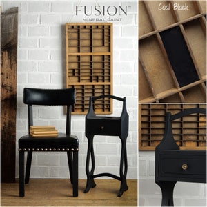 May include: A black side table with a drawer and a curved top rail. The table is painted with Fusion Mineral Paint in the color Coal Black. The table is next to a black chair with a leather seat and nailhead trim. The background is a white brick wall.