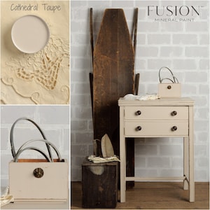 May include: A two-drawer side table painted in Fusion Mineral Paint's Cathedral Taupe color. The table has a distressed finish and is shown in a room with a brick wall. The paint color is shown in a small bowl in the top left corner of the image.