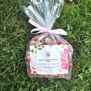 May include: A clear plastic bag filled with dried colorful wildflowers, tied with a light pink ribbon. The white label reads: Cottage Garden Wildflower Potpourri, DO NOT INGEST - Not a culinary product. Contains: Lavender, Larkspur, Calendula, Rose Petals & Yarrow, & other dried flowers.